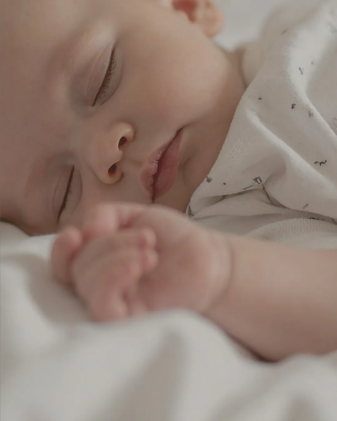 Bebé durmiendo plácidamente boca abajo sobre sábanas blancas