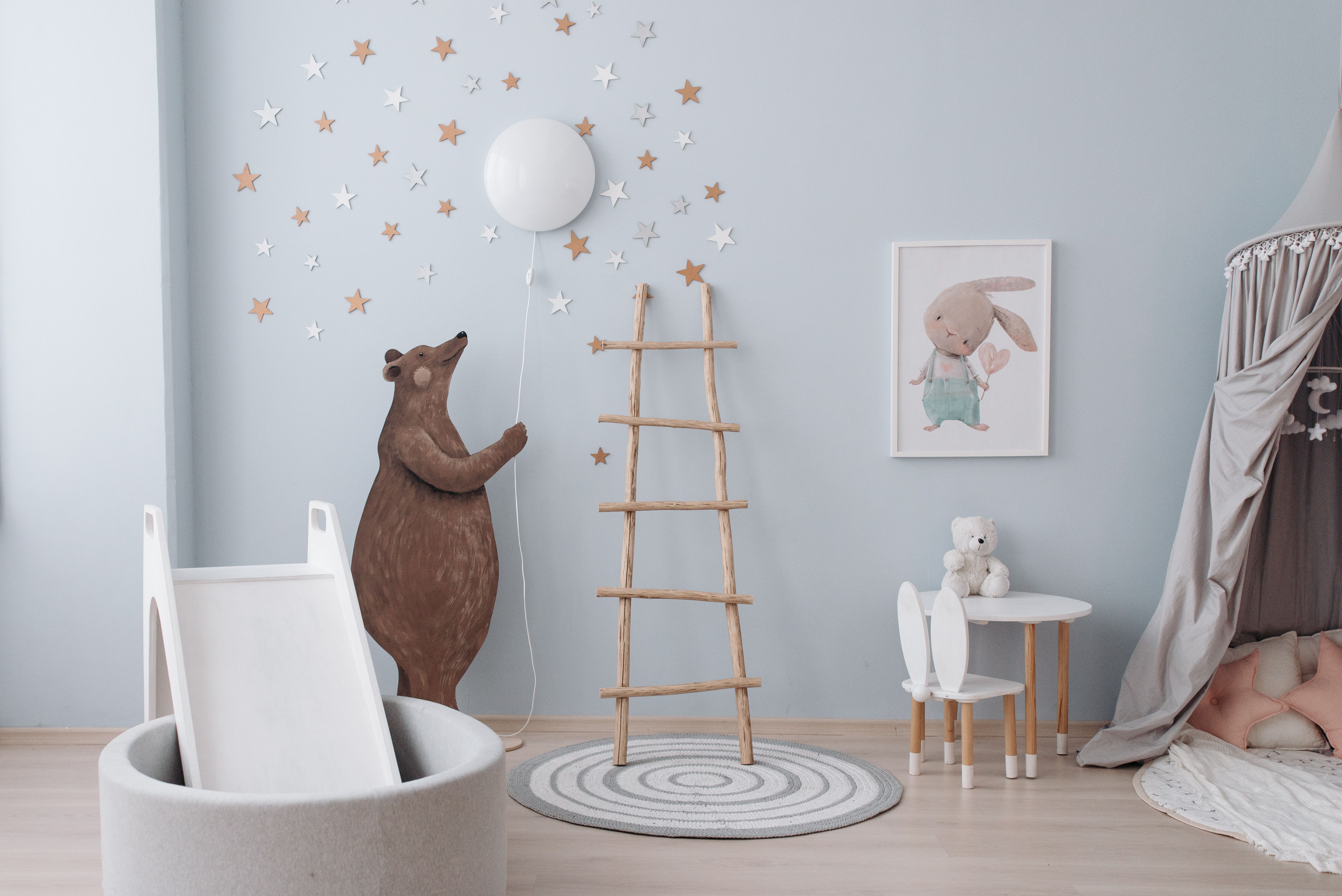 Habitación infantil en tonos azules con un oso de peluche sujetando una lámpara en forma de luna entre estrellas