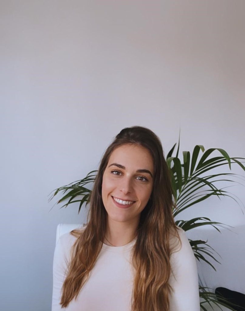 Asesora sueño y crianza infantil, con una planta verde de fondo, sonriendo y relajada